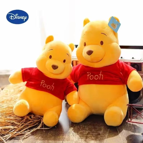 Disney Pooh The Bear plush doll featuring soft yellow fabric, a red shirt, and a friendly smile, suitable for children aged 3 and up.